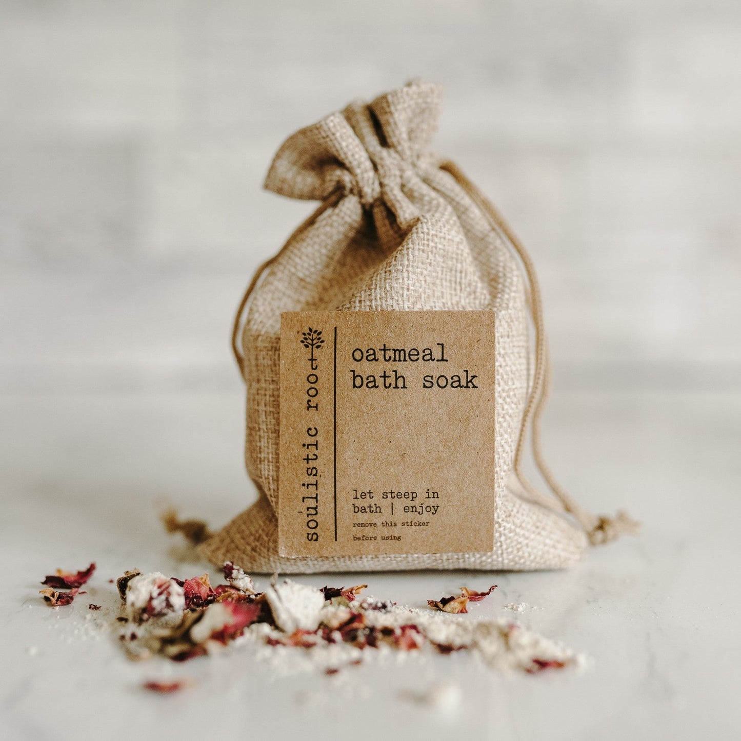 Herbal organic oatmeal bath soak in a burlap bag with some of the contents dumped out showing the oatmeal and rose petals.
