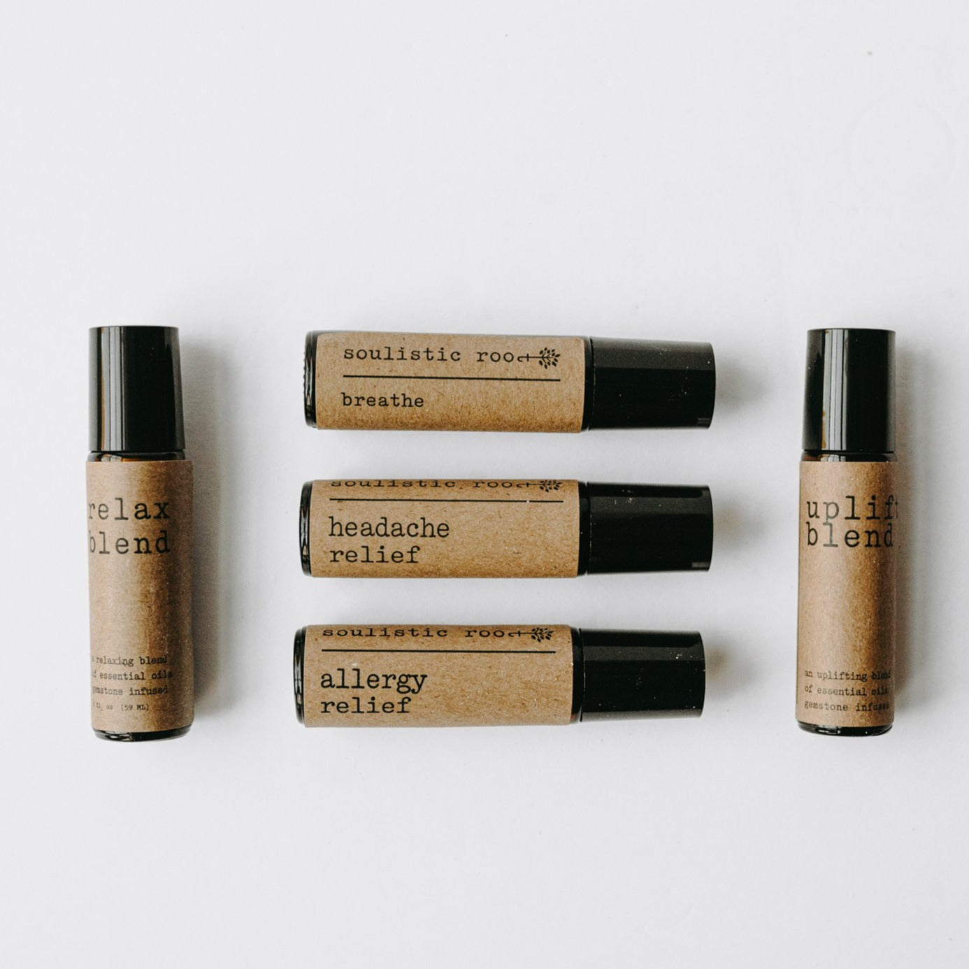 Essential oil rollers. There are five different blends -uplift which has rose quartz gemstones, headache relief, relax blend which has amethyst gemstones, allergy relief and breathe. They are in amber roller bottles in front of a white background.